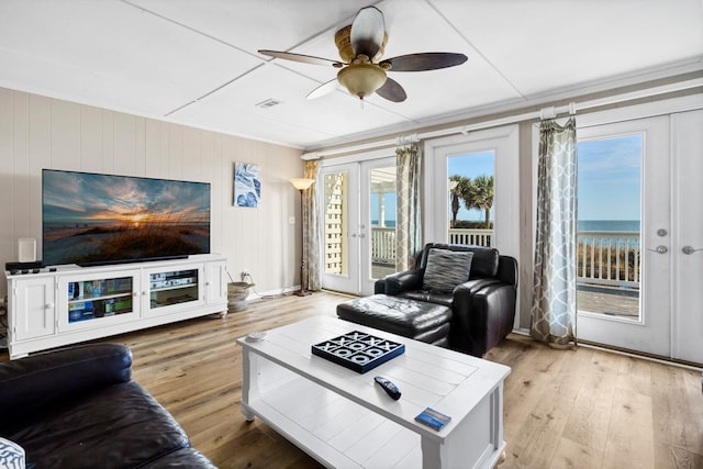 living room featuring ornamental molding, light hardwood / wood-style floors, french doors, and a water view