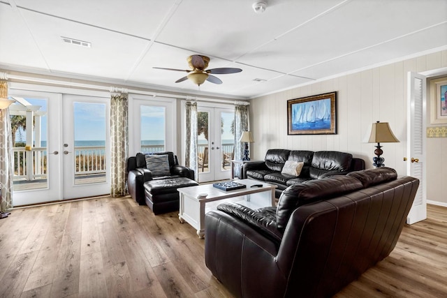 living room with crown molding, a water view, light hardwood / wood-style flooring, and french doors