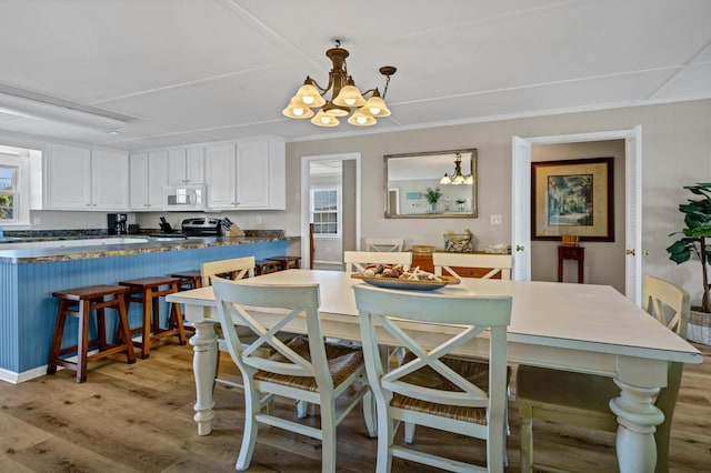 dining space with an inviting chandelier, ornamental molding, and light wood-type flooring