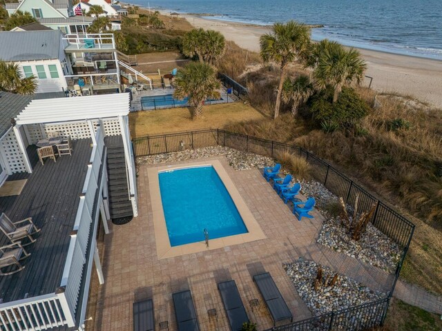 view of swimming pool featuring a water view, a patio area, and a view of the beach