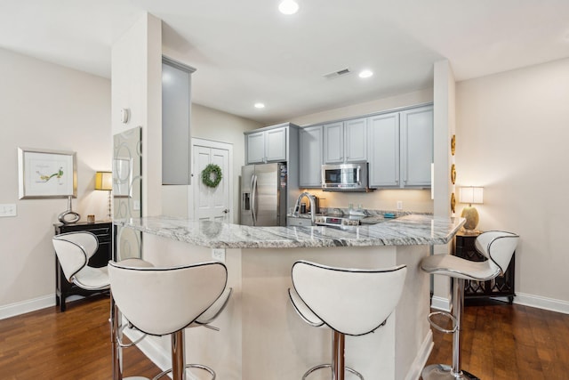 kitchen with stainless steel appliances, dark wood-type flooring, light stone counters, and kitchen peninsula