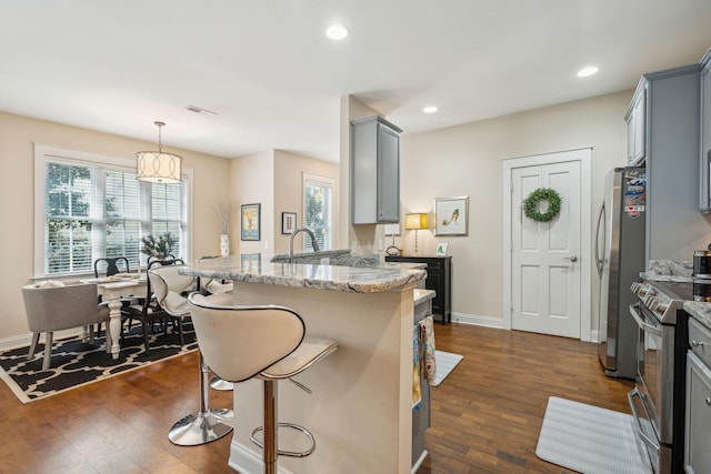 kitchen featuring a breakfast bar, decorative light fixtures, gray cabinetry, stainless steel appliances, and light stone countertops