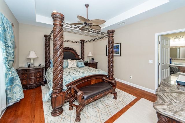 bedroom featuring ceiling fan, a raised ceiling, dark wood-type flooring, and ensuite bath