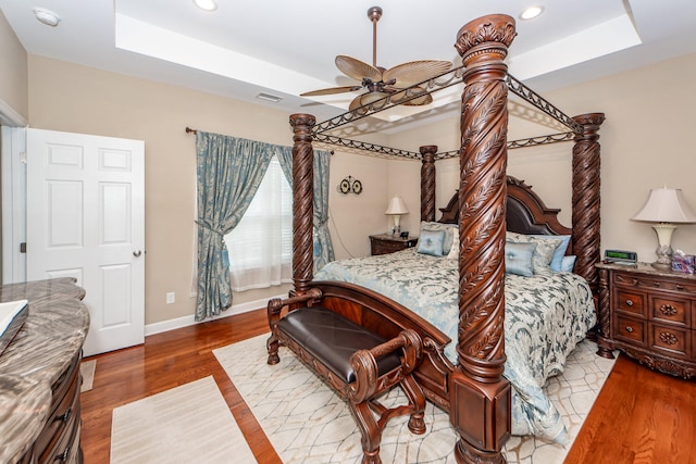 bedroom with hardwood / wood-style flooring, a raised ceiling, and ceiling fan