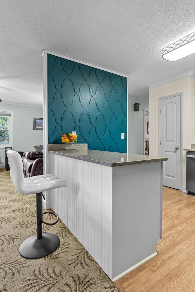 kitchen featuring light wood finished floors, a peninsula, a textured ceiling, stone counters, and dishwasher