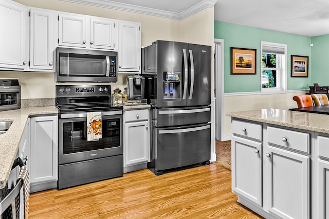 kitchen with ornamental molding, light stone countertops, stainless steel appliances, and light wood finished floors