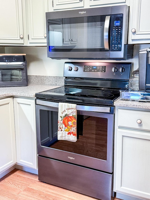 kitchen featuring light wood-style flooring, appliances with stainless steel finishes, a toaster, and white cabinetry