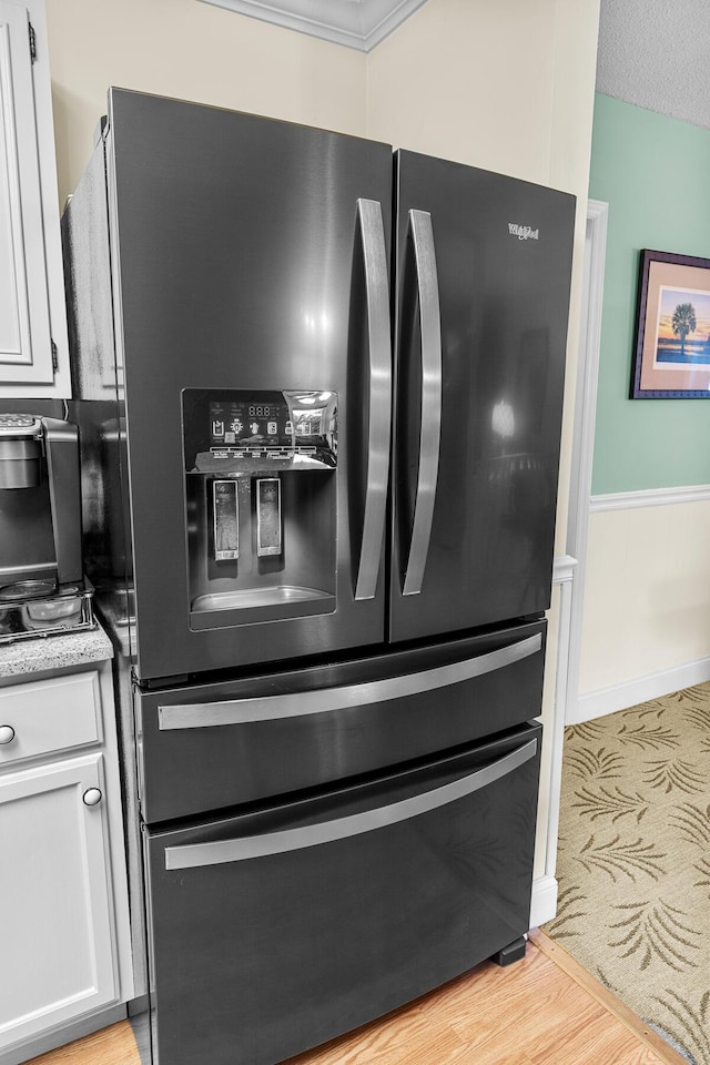 details featuring white cabinets, wainscoting, light wood-type flooring, black refrigerator with ice dispenser, and light stone countertops