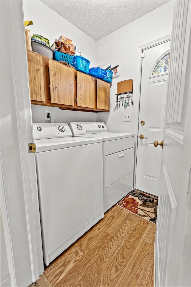 laundry area with washing machine and dryer, cabinet space, a textured ceiling, and light wood finished floors
