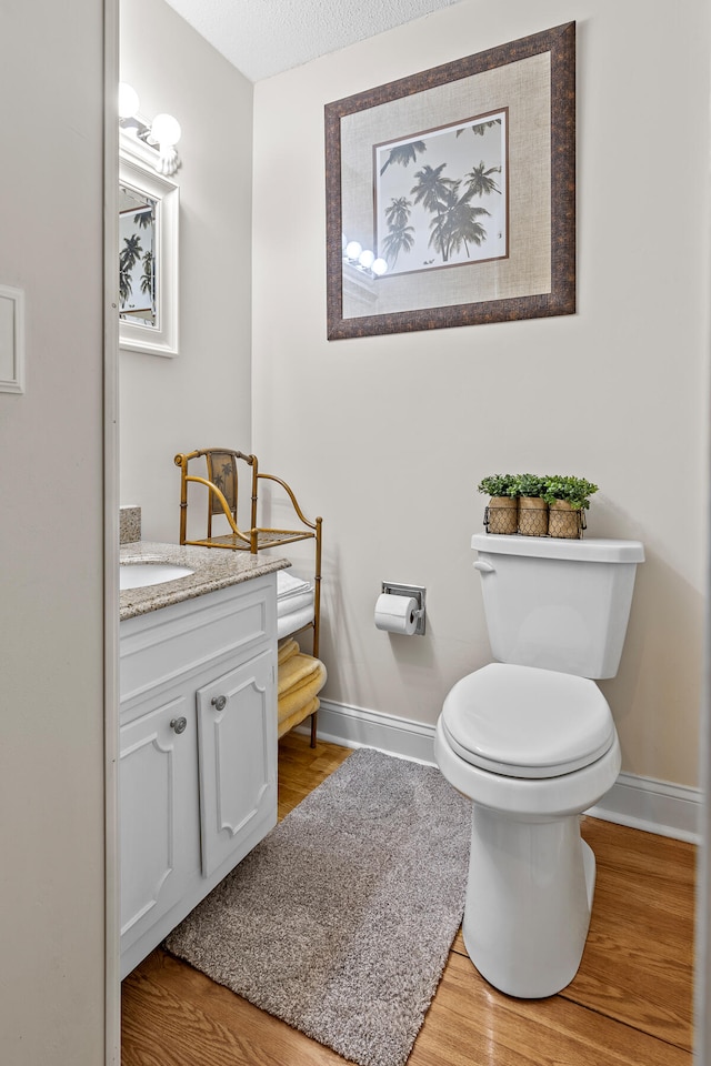 bathroom with a textured ceiling, wood-type flooring, vanity, and toilet