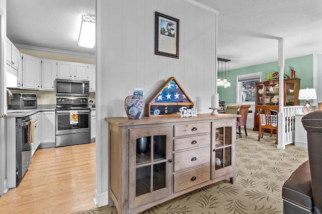 kitchen with white cabinets, light hardwood / wood-style flooring, decorative light fixtures, stainless steel appliances, and crown molding