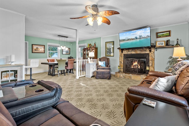 living area with carpet floors, crown molding, a stone fireplace, and ceiling fan with notable chandelier