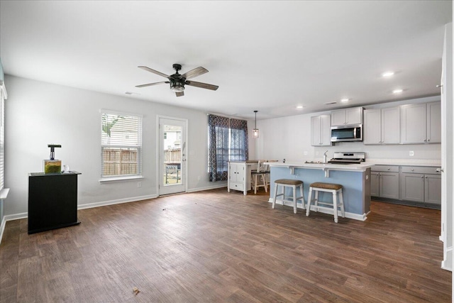 kitchen with dark hardwood / wood-style flooring, a center island with sink, appliances with stainless steel finishes, a kitchen bar, and ceiling fan