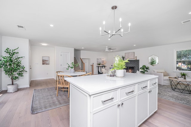 kitchen featuring white cabinets, light hardwood / wood-style floors, hanging light fixtures, and a fireplace