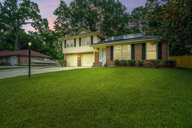 tri-level home with a lawn, solar panels, and a garage