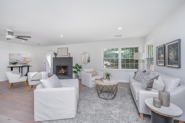 living room with ceiling fan, light hardwood / wood-style floors, and a brick fireplace