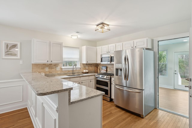 kitchen with appliances with stainless steel finishes, kitchen peninsula, sink, and white cabinets