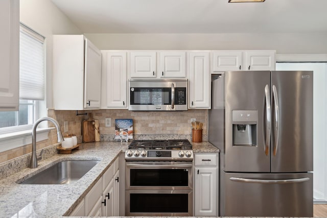 kitchen with sink, appliances with stainless steel finishes, backsplash, light stone counters, and white cabinets