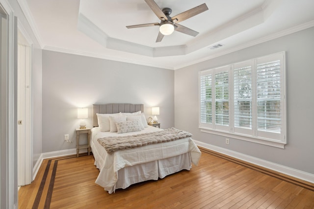 bedroom with ornamental molding, light hardwood / wood-style flooring, ceiling fan, and a tray ceiling