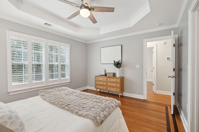 bedroom with crown molding, hardwood / wood-style floors, ceiling fan, and a tray ceiling