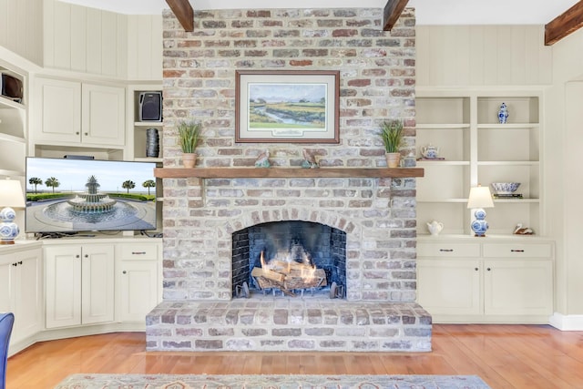 living area with beam ceiling, light wood-style floors, built in shelves, and a fireplace