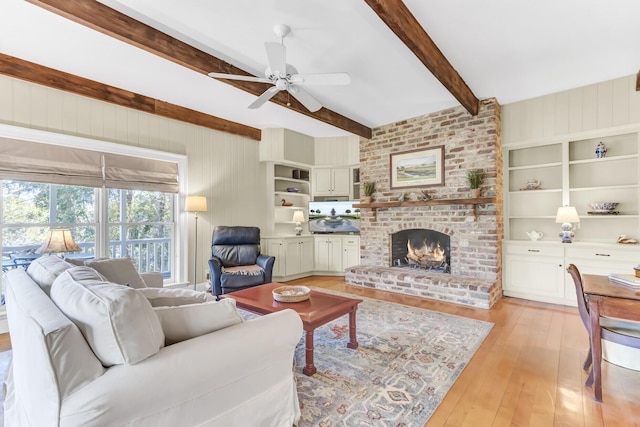 living area featuring beam ceiling, a ceiling fan, built in features, light wood-style floors, and a fireplace