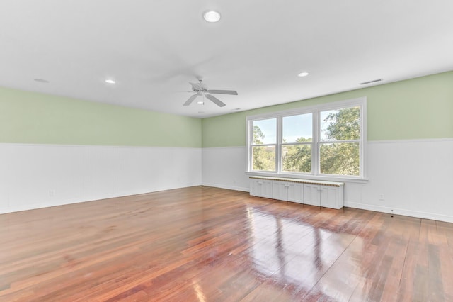 unfurnished room with visible vents, wainscoting, radiator heating unit, and wood finished floors