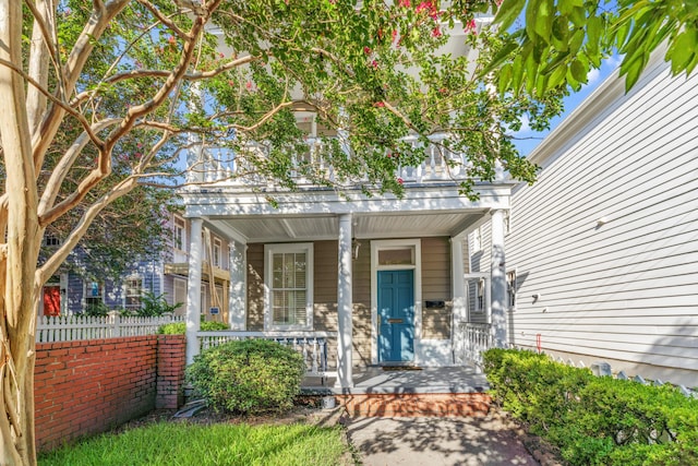 view of exterior entry with covered porch and fence