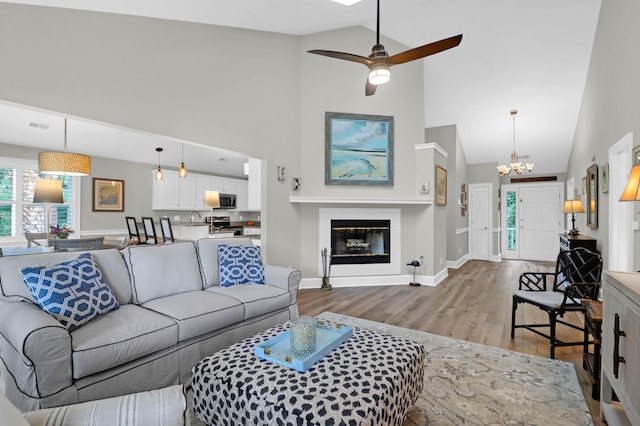 living room featuring high vaulted ceiling, sink, ceiling fan with notable chandelier, and light wood-type flooring