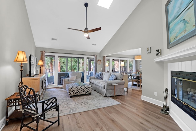 living room featuring wood-type flooring, ceiling fan, high vaulted ceiling, and a skylight