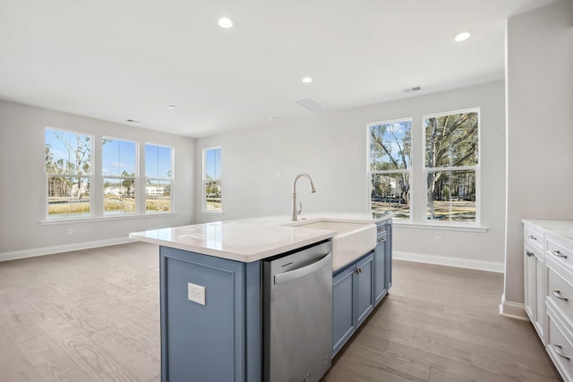 kitchen with light wood-type flooring, a center island with sink, stainless steel dishwasher, and plenty of natural light