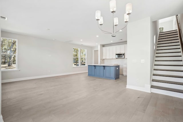 unfurnished living room featuring a chandelier, light wood-type flooring, and sink