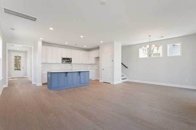 kitchen with hanging light fixtures, blue cabinetry, light hardwood / wood-style floors, white cabinetry, and a chandelier