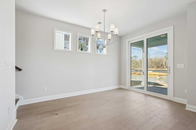 empty room with light hardwood / wood-style floors and an inviting chandelier