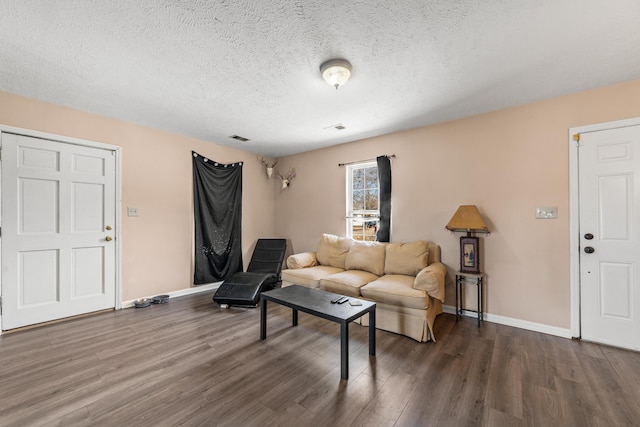 living area with a textured ceiling, wood finished floors, visible vents, and baseboards