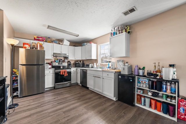 kitchen with stainless steel appliances, light countertops, visible vents, dark wood-type flooring, and under cabinet range hood