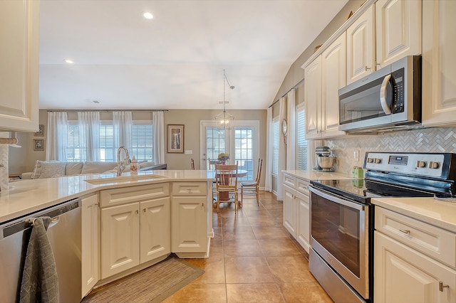 kitchen featuring sink, lofted ceiling, decorative light fixtures, light tile patterned floors, and appliances with stainless steel finishes