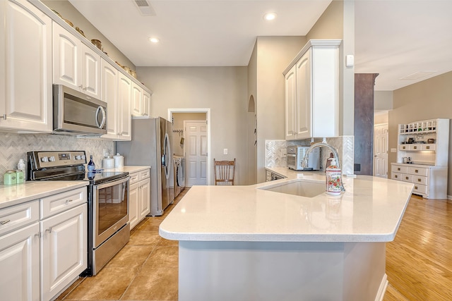 kitchen featuring decorative backsplash, appliances with stainless steel finishes, sink, white cabinets, and washing machine and dryer