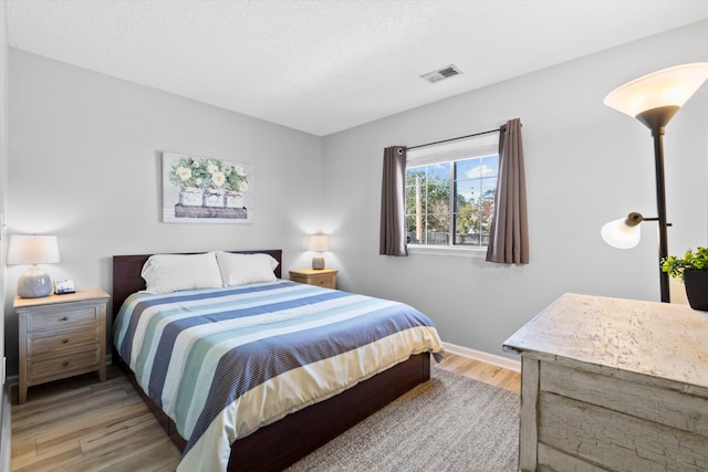 bedroom featuring baseboards, visible vents, a textured ceiling, and light wood-style floors