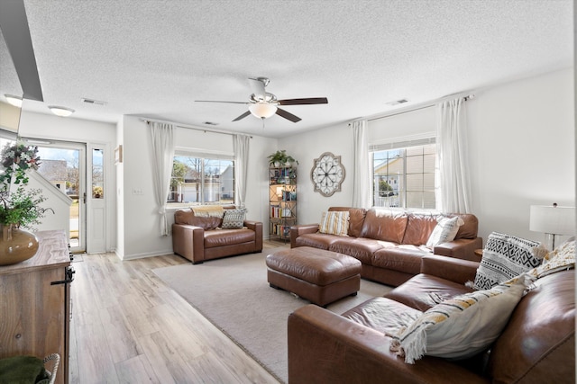 living area featuring visible vents, a textured ceiling, light wood-type flooring, and a ceiling fan