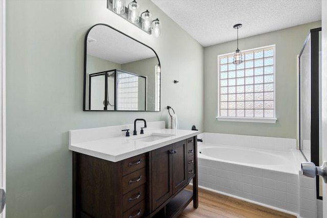 bathroom featuring a shower stall, vanity, wood finished floors, a bath, and a textured ceiling