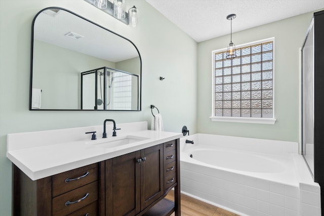 full bath with visible vents, a textured ceiling, wood finished floors, a bath, and vanity