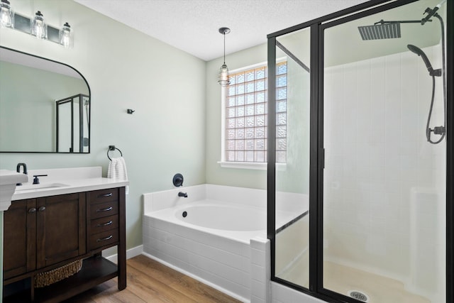 bathroom with a stall shower, a textured ceiling, wood finished floors, a bath, and vanity