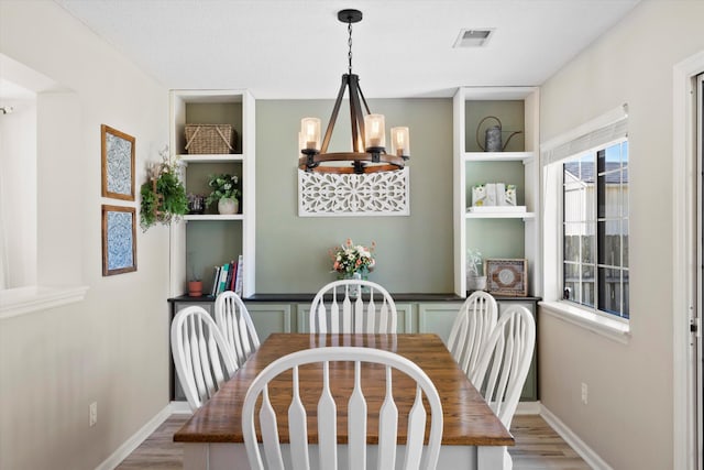 dining space with visible vents, built in features, wood finished floors, an inviting chandelier, and baseboards