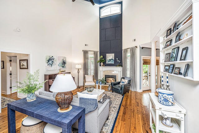 living room featuring a high ceiling, a glass covered fireplace, wood finished floors, ornate columns, and visible vents