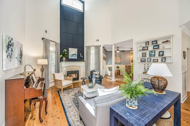 living area with ceiling fan, a glass covered fireplace, light wood-style flooring, a towering ceiling, and visible vents