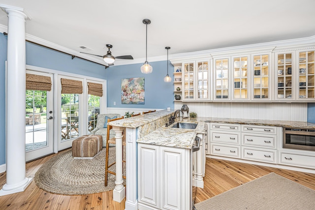kitchen featuring crown molding, a peninsula, stainless steel oven, ornate columns, and a sink