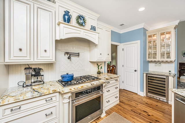 kitchen with light stone counters, beverage cooler, light wood-style flooring, stainless steel appliances, and backsplash