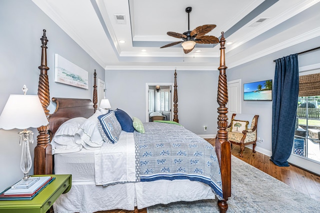 bedroom with visible vents, crown molding, baseboards, a raised ceiling, and wood-type flooring