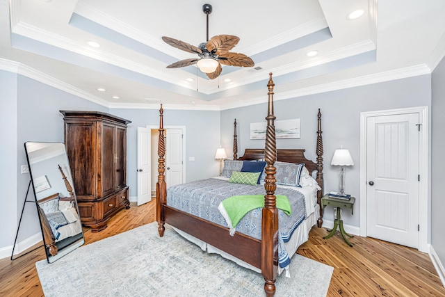 bedroom featuring light wood-style floors, ornamental molding, and a raised ceiling